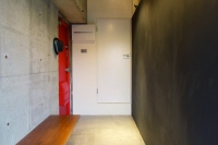 事例1：ベンチ付きのエントランス。印象的な朱赤の玄関扉は奥様選定。向かいの壁には黒板塗料を塗装し、家族や来客のコミュニケーションを図るスペースとしても機能を持たせた。正面の扉はトイレにつながり、回遊性のある間取りとなっている。